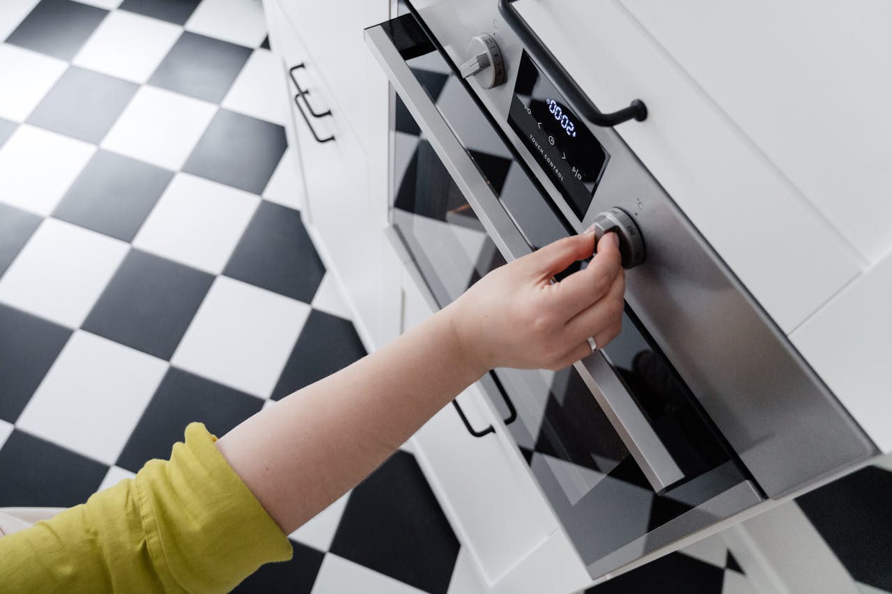 Hand adjusting the temperature dial on a modern stainless steel oven in a contemporary kitchen.