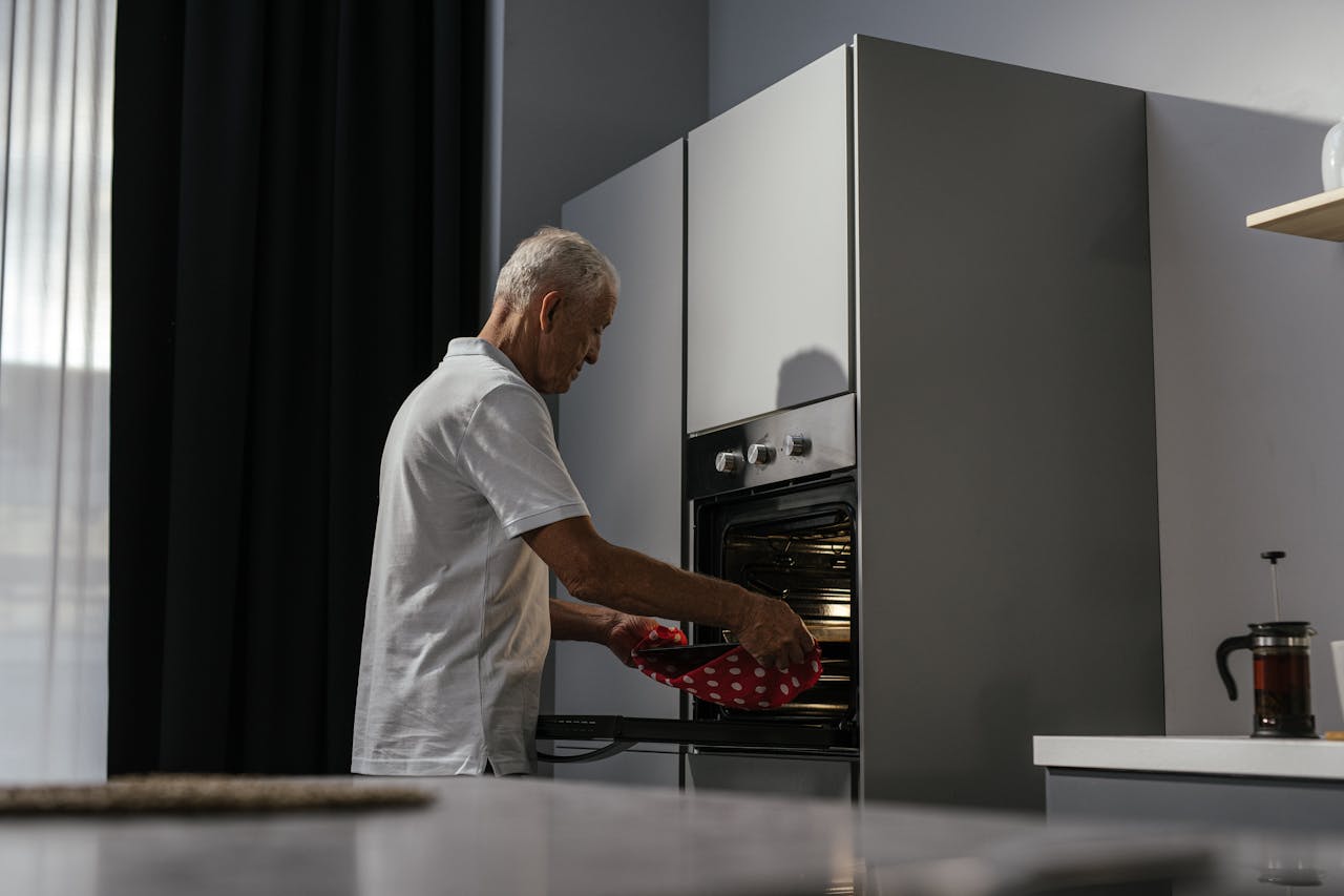 Elderly man using oven in a modern kitchen interior with a focus on light and shadows.